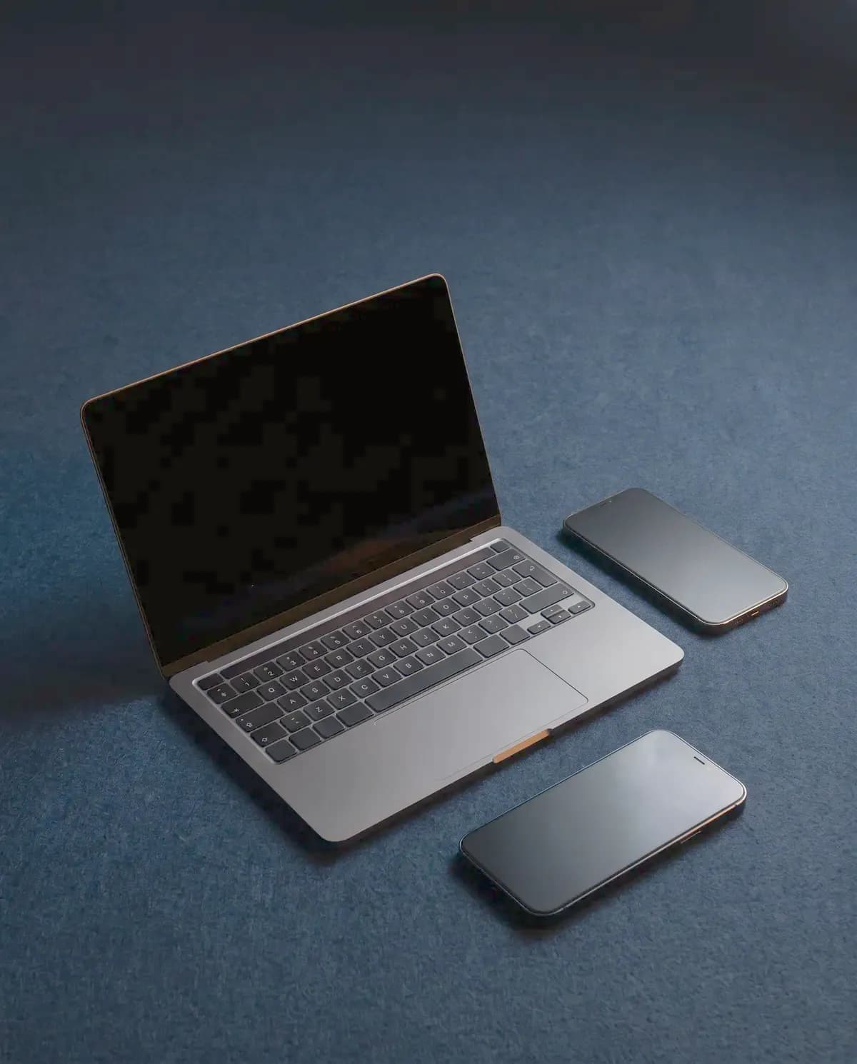 Illustrative photograph of a laptop and smartphones on navy felt
