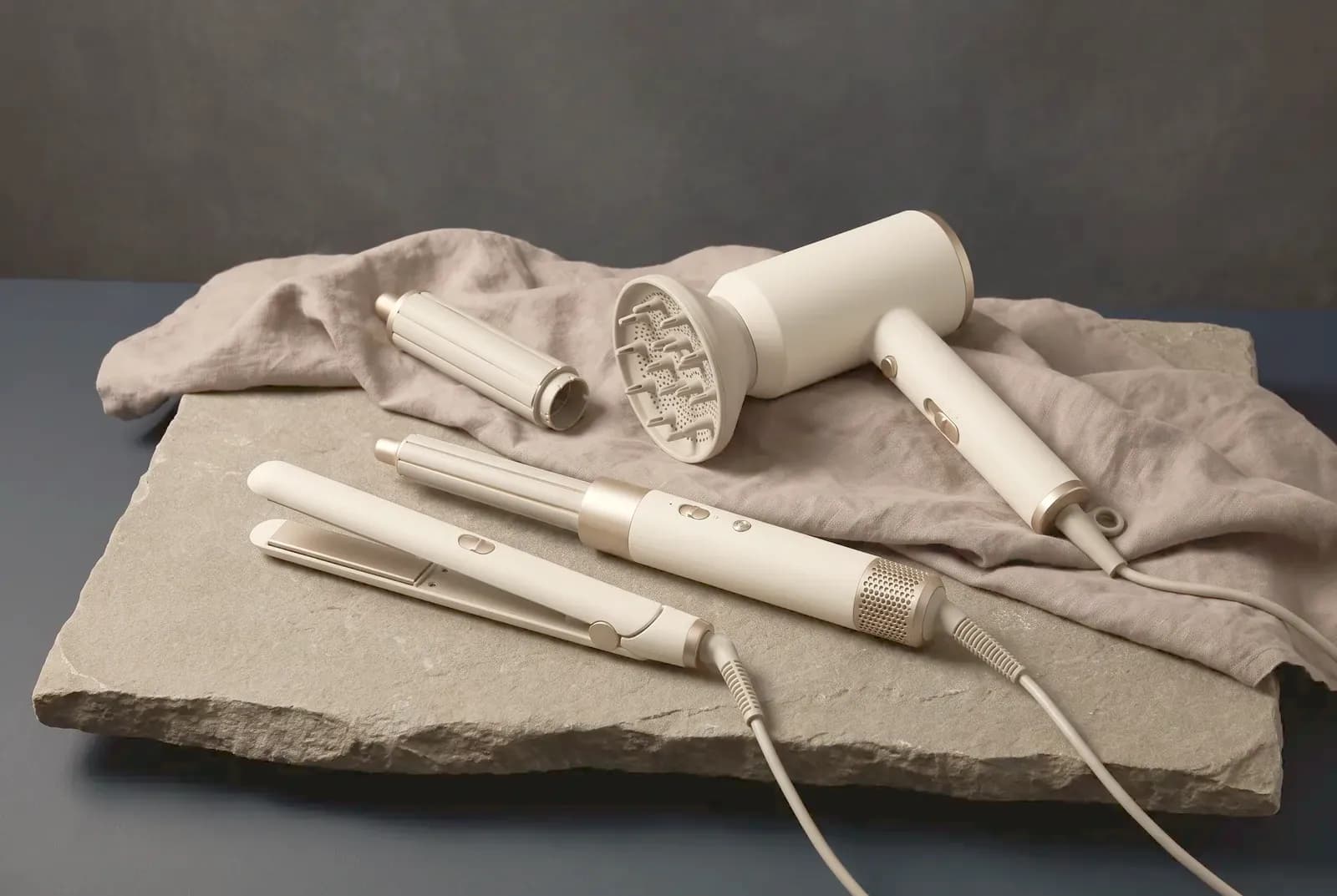 A hair dryer, straightener and air styler with attachments on warm grey stone