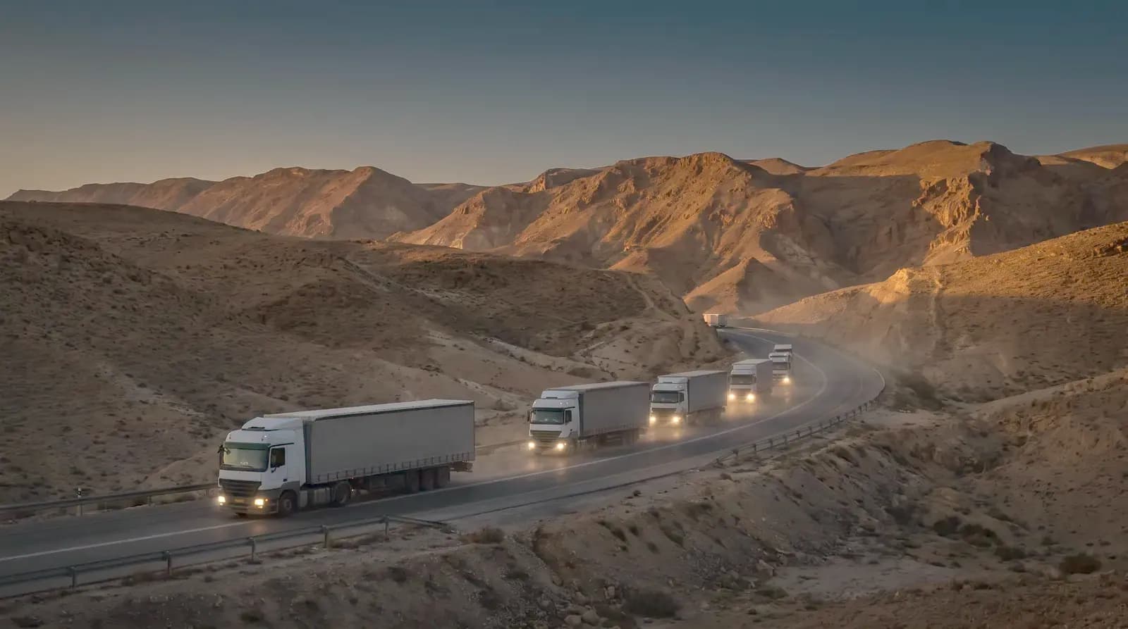 Truck convoy on a desert highway at dusk